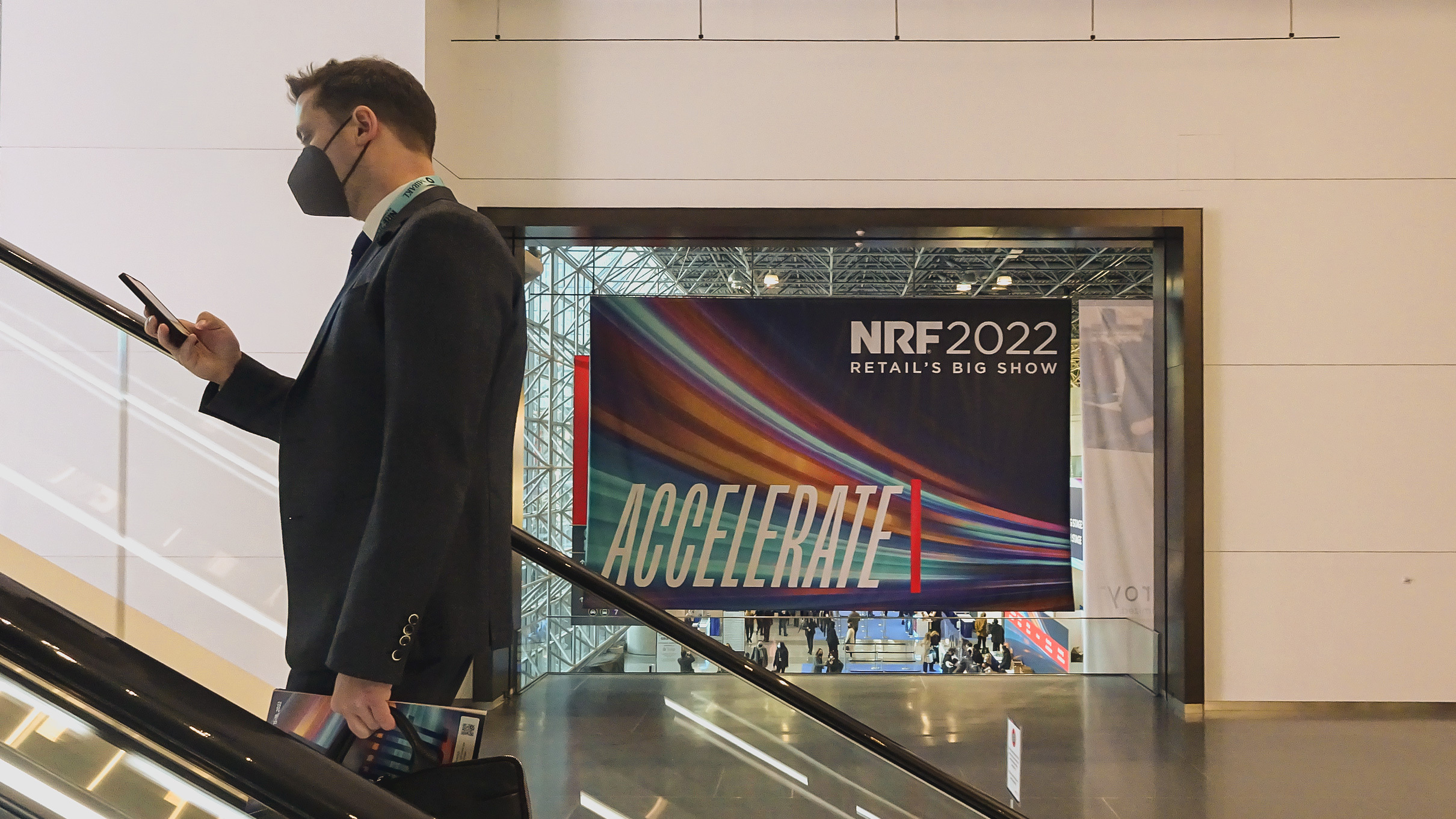 Man on escalator with banner in the background saying "Accelerate" - the theme of the retail trend show by the NRF